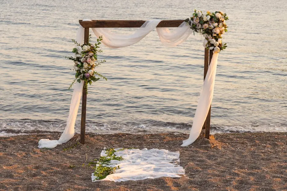 A beautifully decorated wedding arch on a sandy beach, framed by gentle waves and a clear blue sky, perfect for a ceremony.